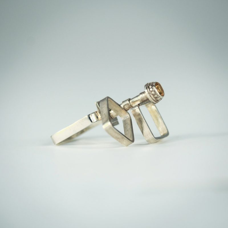 This is a stunning Kinetic Square Cocktail Ring! It has a square ring shank, sparkling citrine stone set in a decorative bezel, 2 square rings on top that like to spin around and will keep you and everyone around you mesmerized! Made from sterling silver and has a polished finish for a luscious look. Side view.